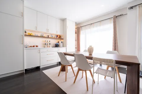 Pantry cabinetry in warm white with lit open display shelving at its centre, beside the dining table