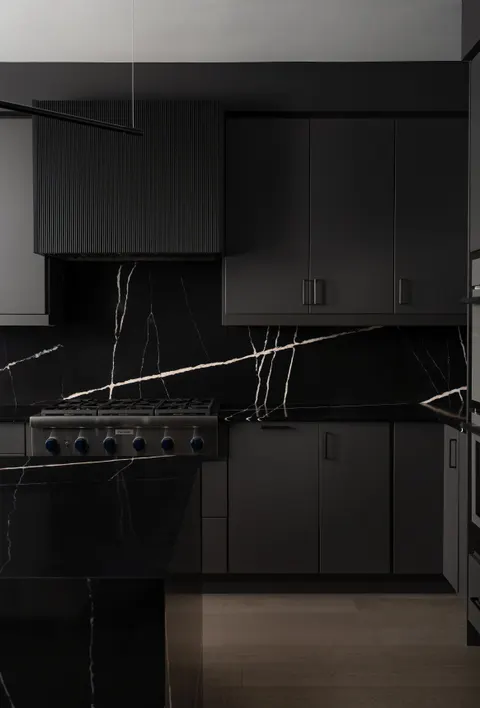 The black marble backsplash behind a stainless range top, under charcoal fluted and slab cabinets
