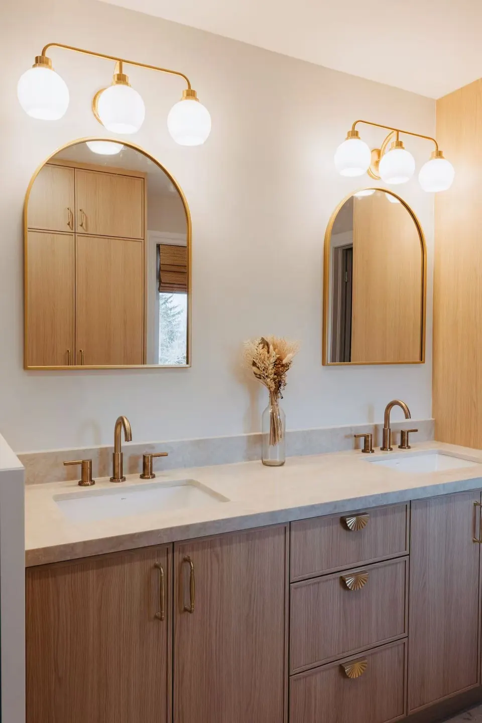Oak shaker double vanity with scalloped brass pulls under two arched brass mirrors and globe light bars