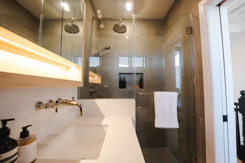 Bathroom with a floating oak vanity, a backlit mirror shelf and wall-mounted brass taps, glass shower behind