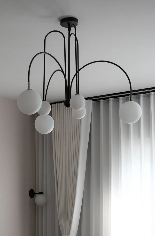 The black arched chandelier, its glass globes hanging in front of pleated sheer curtains