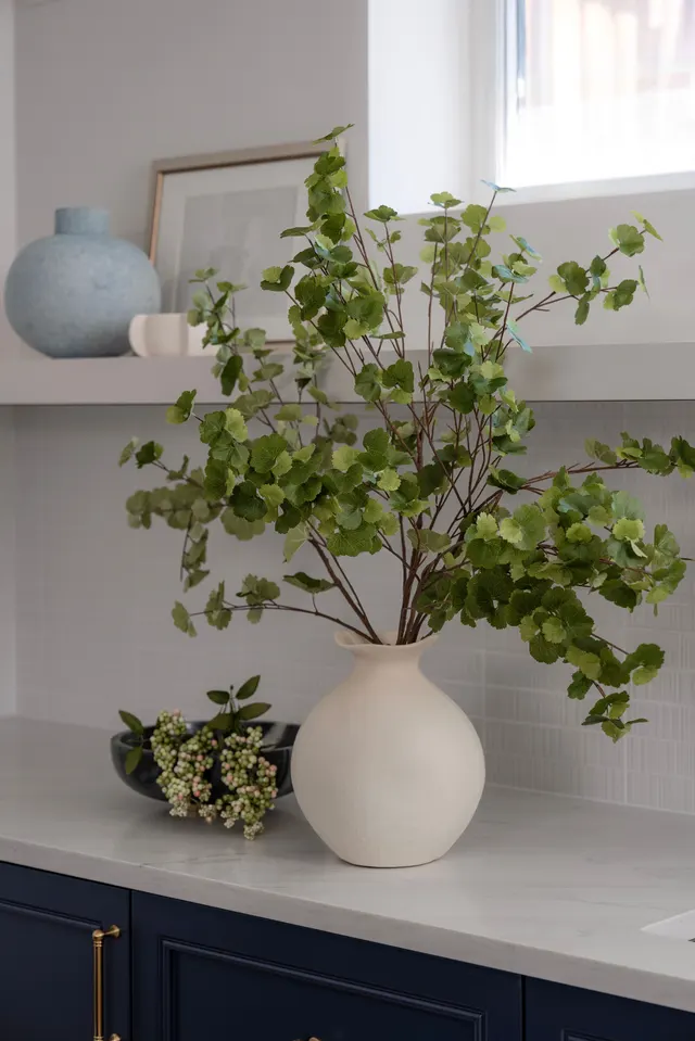 Branches in a white vase on a stone counter above navy cabinets