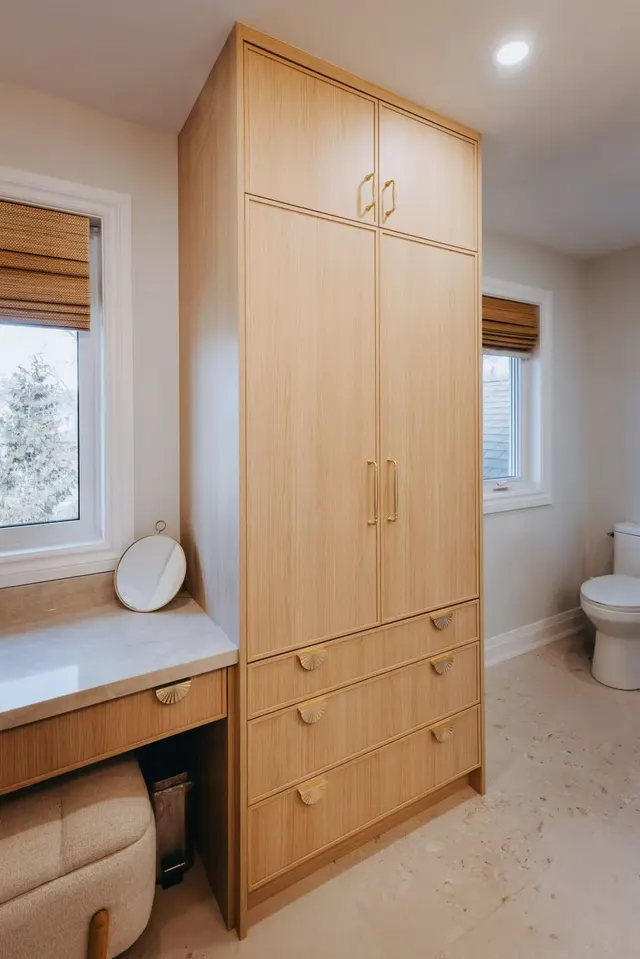 Floor-to-ceiling oak linen tower beside a makeup counter in a primary ensuite