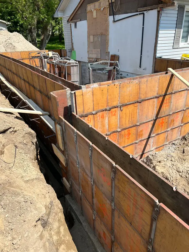 Foundation wall forms set in the trench beside the house