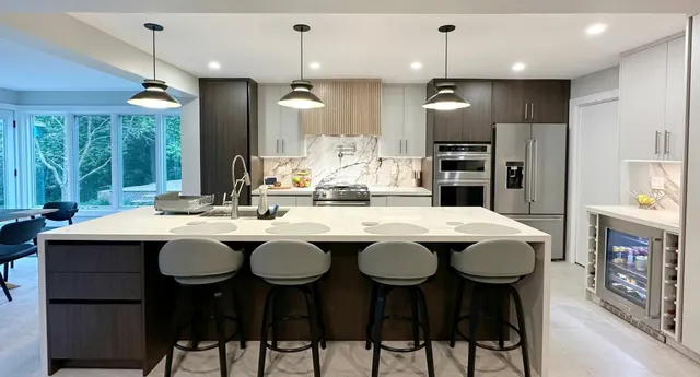 Kitchen with a white waterfall island and bar stools under black pendants, dark oak cabinetry behind