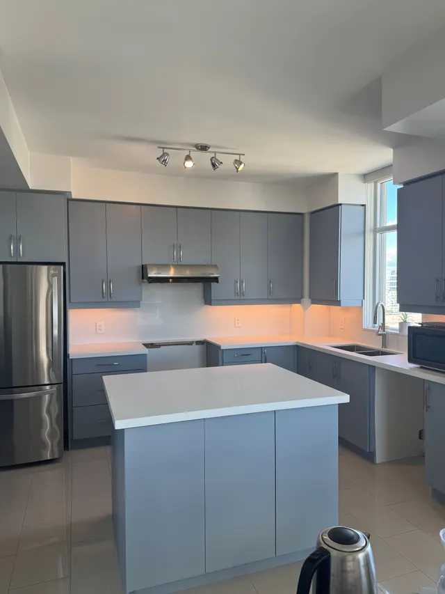 Condo kitchen with grey cabinets, a white quartz island and stainless appliances under track lighting
