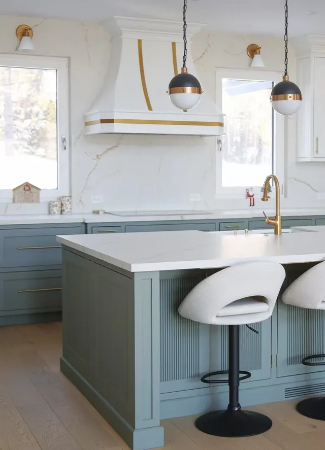 Sage-green island with white swivel stools under brass pendants