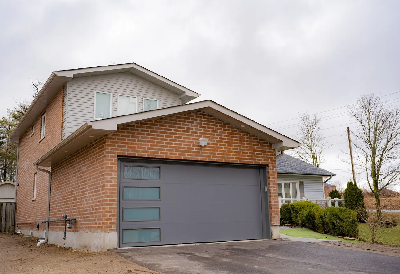 A finished three-storey addition in red brick and grey siding over a charcoal glass-panel garage door